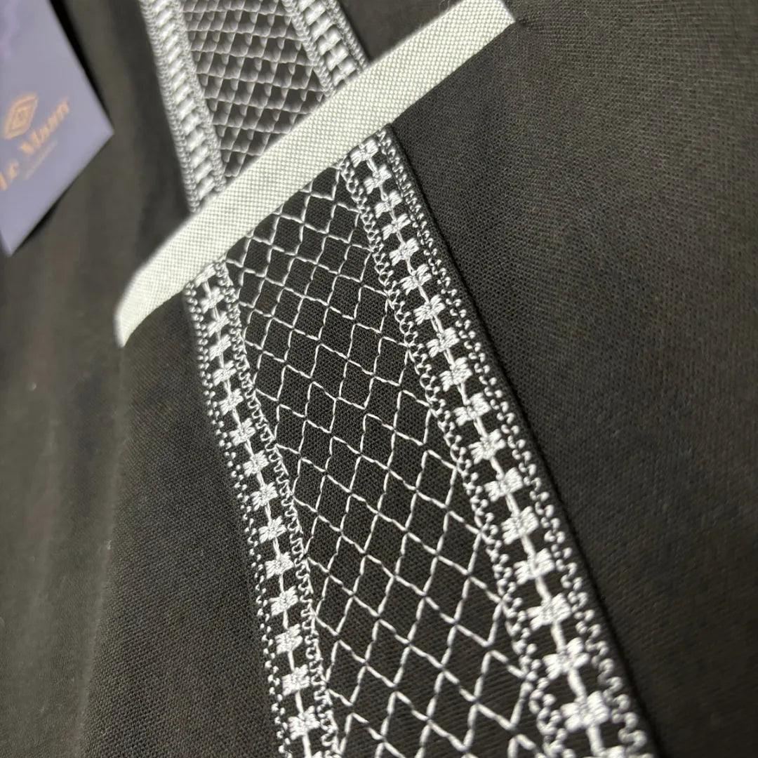 Primer plano del bordado artesanal en forma de panal color gris sobre tela de 100% algodón negro, resaltando la precisión de la costura y el diseño de vanguardia